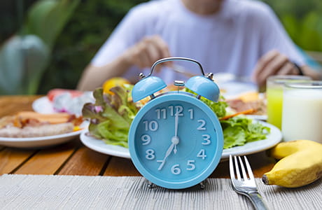 an image of a blue alarm clock with a person in the background eating a healthy meal