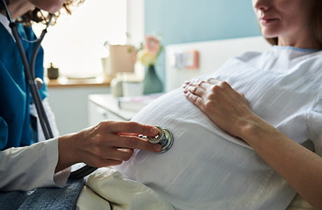 A member of a pregnant woman's childbirth care team examines her belly with a stethoscope