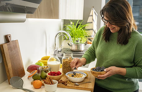 A woman smiling as she adds berries on top of her cereal.