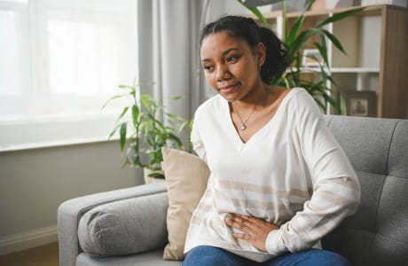 A woman sitting on a couch feeling uncomfortable pain in her stomach