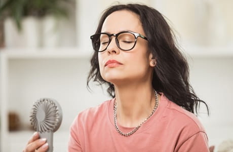 A woman cooling off by using a hand held fan