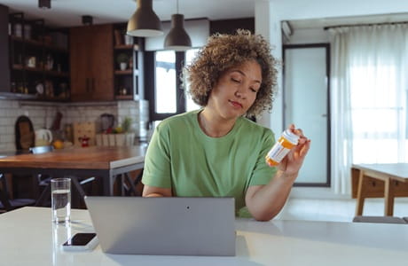 Mature African American woman sitting at a table looking at her prescription. 