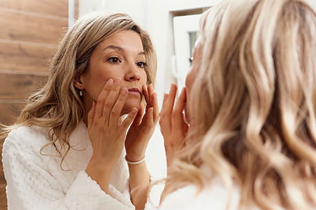 Person examining facial skin in a mirror as part of a healthy skincare routine.