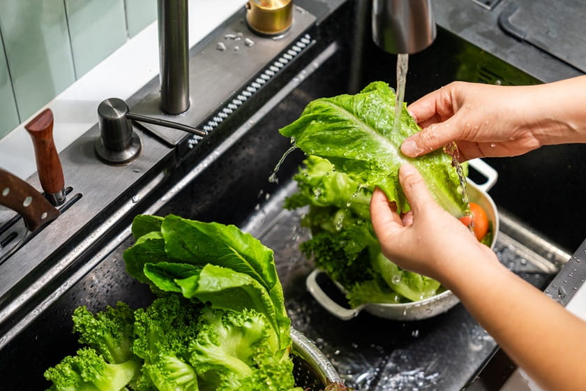 A person washing greens and lettuce under running water to help decrease the chances of cyclospora infection