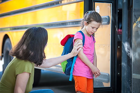 Student boarding a school bus with support from a caregiver, illustrating the transition back to school.