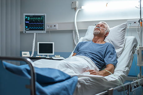 Patient resting in a hospital bed with monitoring equipment visible beside the bed.