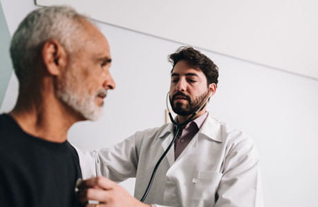 A male doctor listening to an older mans heart