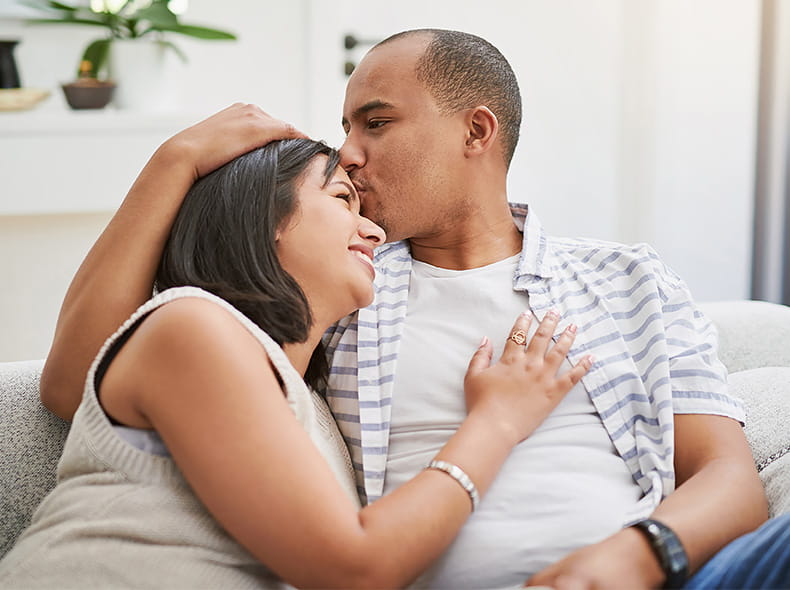 A young couple seated on a couch shares an affectionate moment.