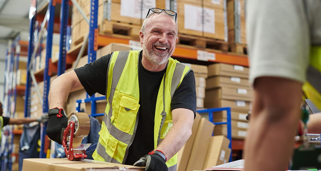 A man in a warehouse smiling while taping a box.