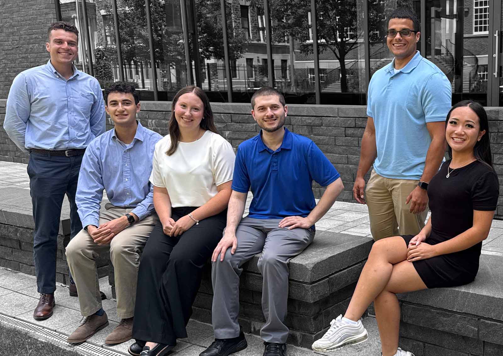Group of students gathered outdoors on a campus plaza in front of a modern academic building.