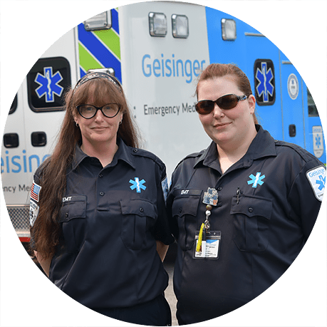 Two emergency medical services team members standing in front of a Geisinger ambulance.
