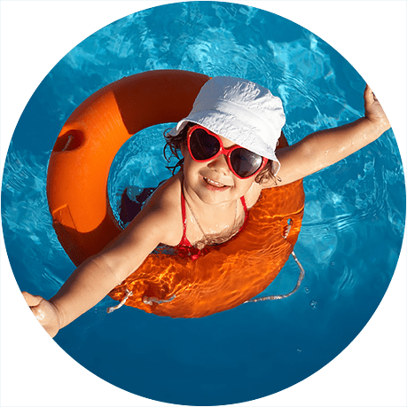 Child wearing a flotation ring and sun hat while swimming in a pool, illustrating summer water safety.