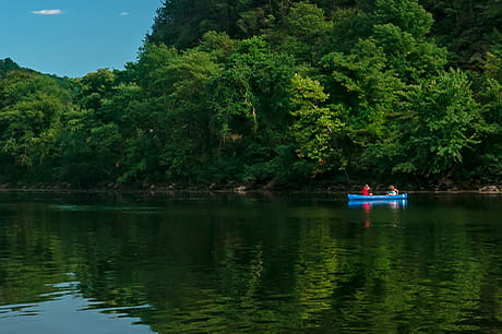 A blue canoe is paddled down a river in the summer.