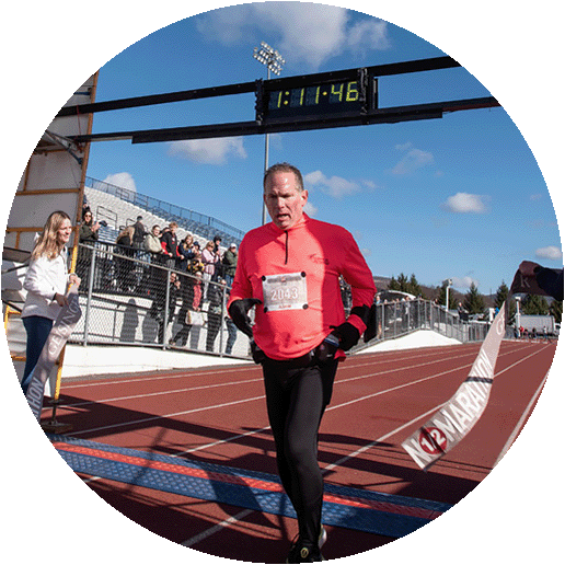 A middle-aged man is running in a road race and crosses the finish line.