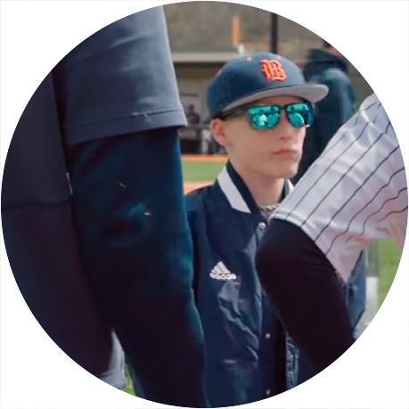 Young baseball player wearing sunglasses and team cap standing on the field during a youth sports game or practice.