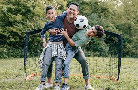 a dad playing soccer with his two sons