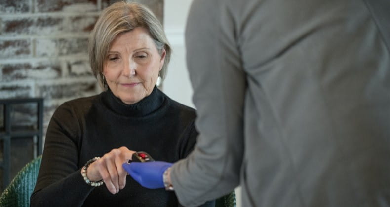 older lady sitting in a chair at home while a nurse checks her blood oxygen levels