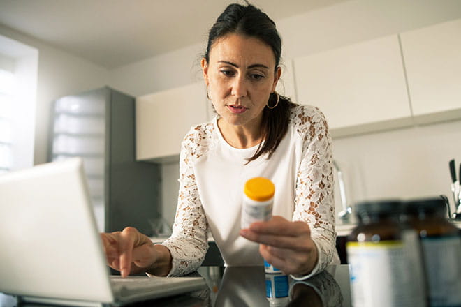 woman on computer while reading her pill bottle 